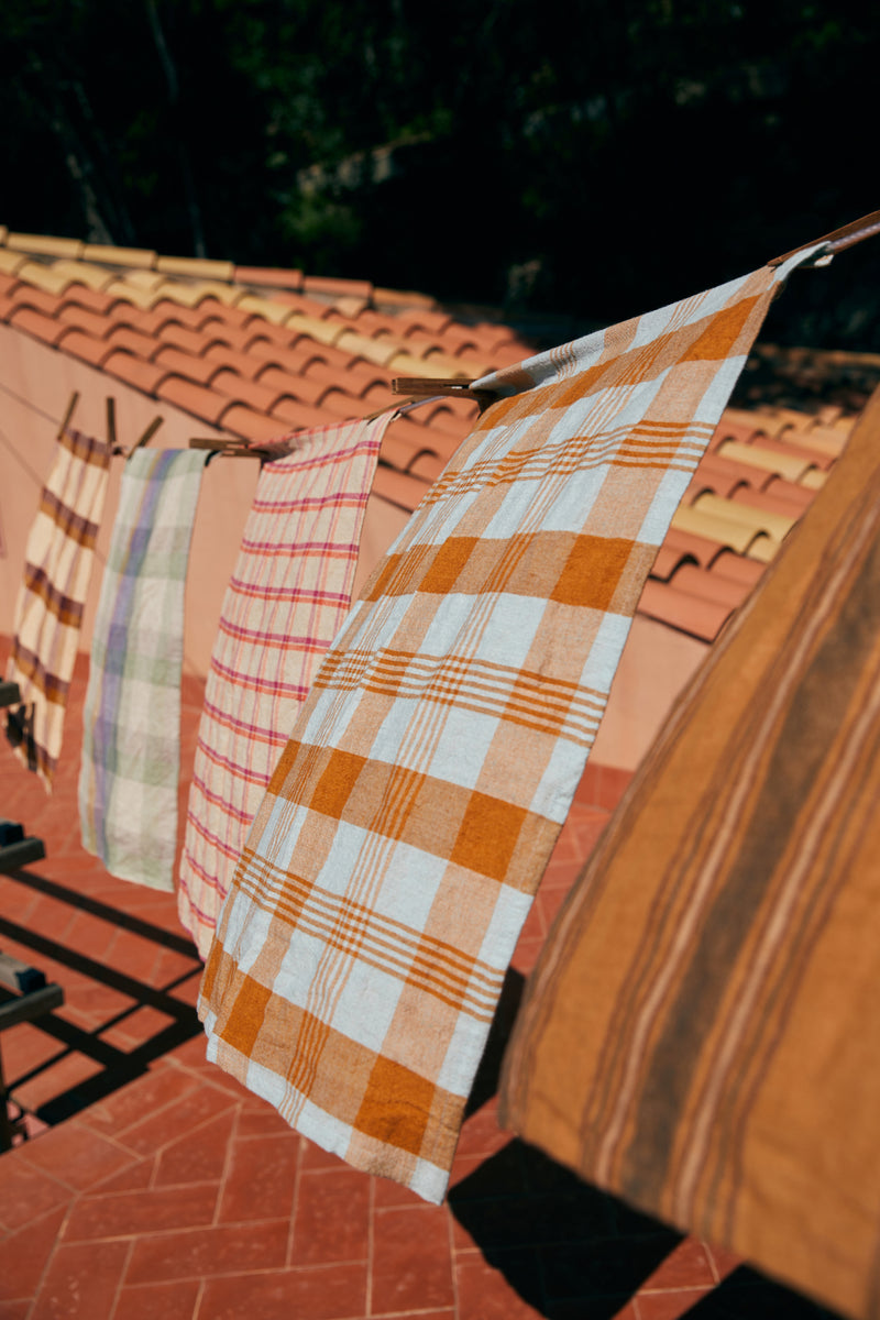 Plaid and striped cloths hanging on a clothesline against a tiled roof.
