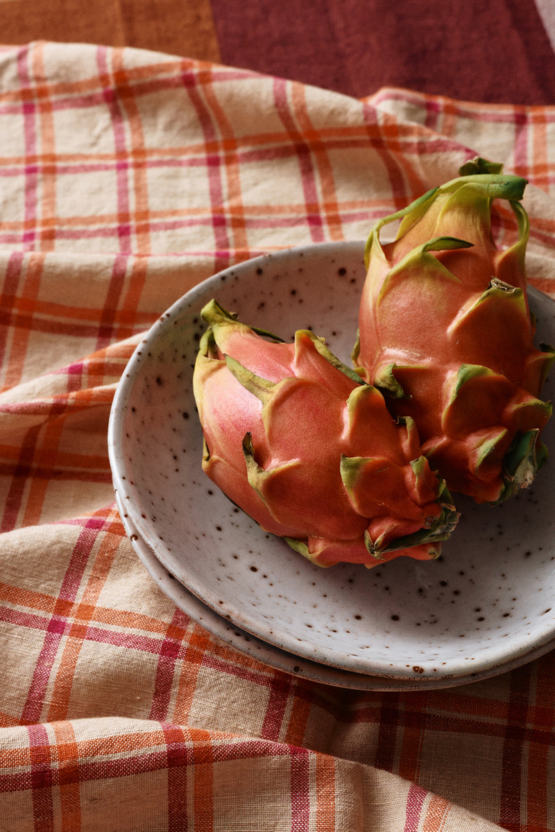 Two dragon fruits on a speckled ceramic plate with a plaid cloth background