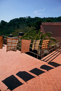 Sunlit terrace with checkered towels and shadows on a red brick floor.