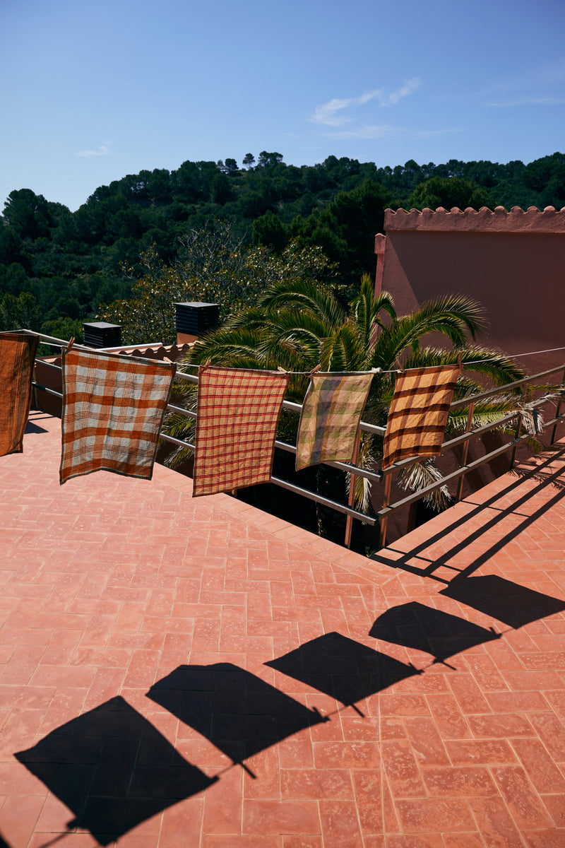 Sunlit terrace with checkered towels and shadows on a red brick floor.