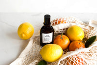 Bottle of Caudalie skincare product with lemons and oranges on a white background