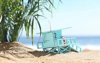 Miniature lifeguard stand on a sandy beach with palm leaves and ocean in the background