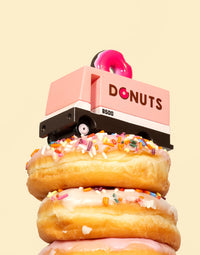 Stack of donuts with a pink donut press labeled 'DONUTS' on a beige background