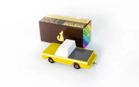 Yellow toy truck with a white bed next to a brown box on a white background