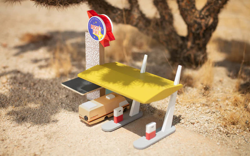 Toy gas station set in a desert landscape with a toy truck at the pump.
