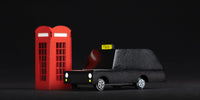 Model of a black taxi with a yellow 'Taxi' sign next to two red telephone booths on a black background