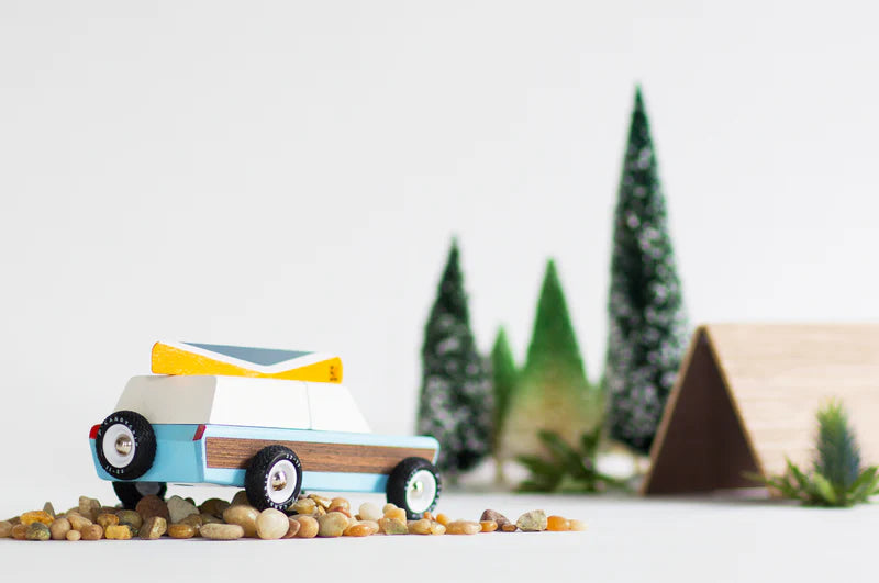 Toy camper with a small tent and trees in the background on a light surface