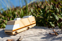 Wooden toy van on a sandy surface with greenery in the background