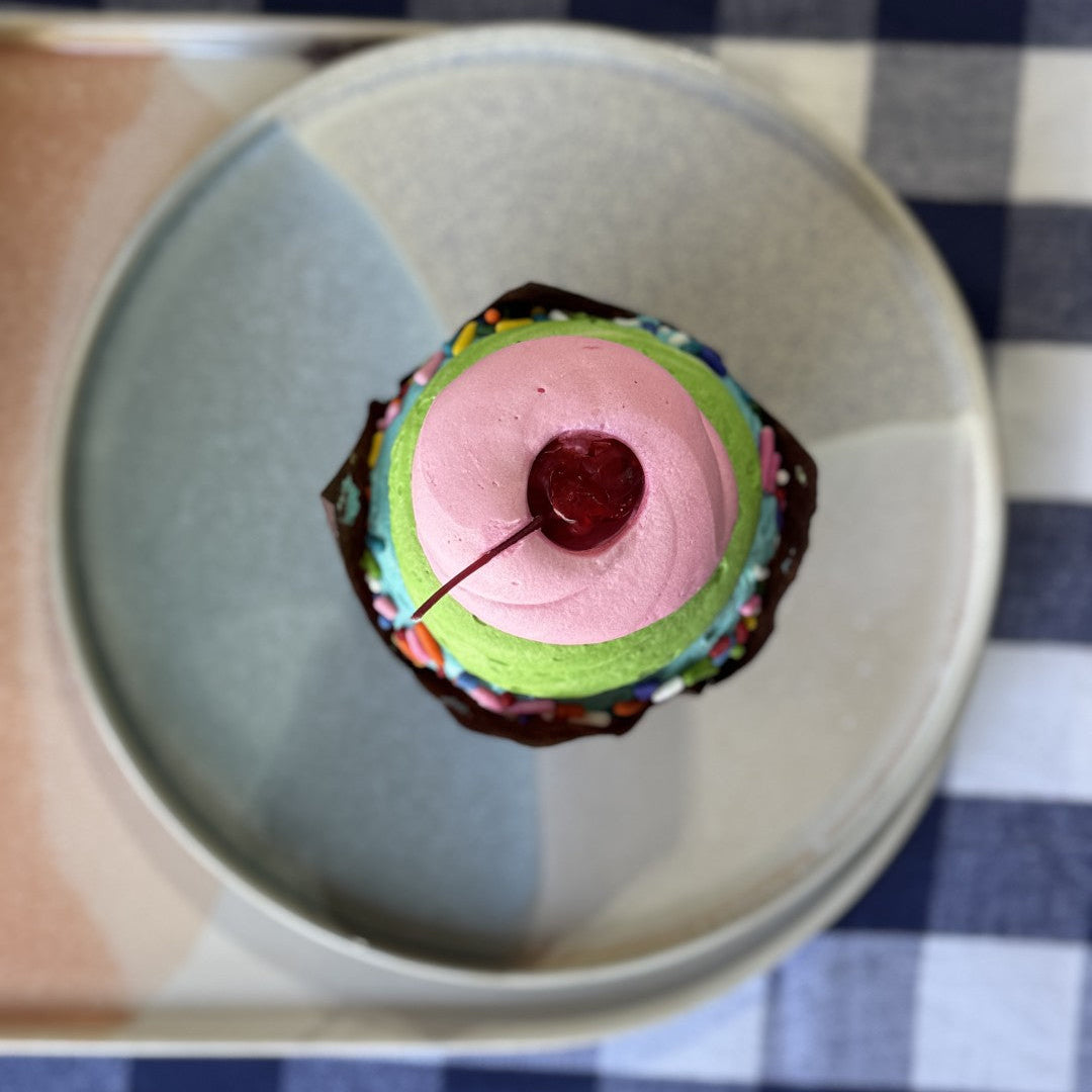 Colorful layered dessert with a cherry on top on a checkered tablecloth