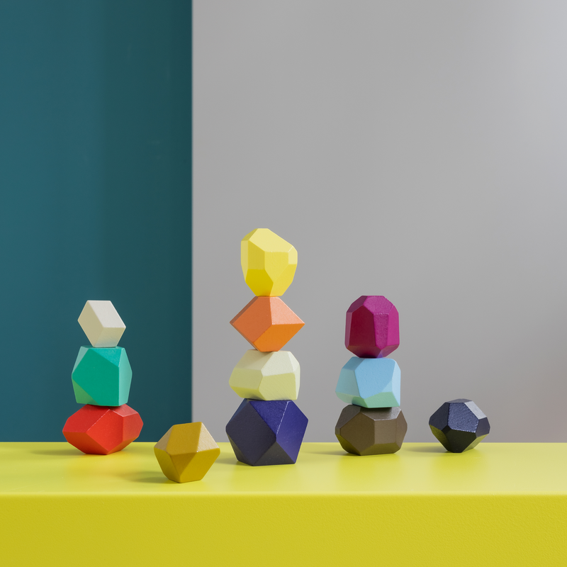 Colorful geometric stone stacks on a yellow surface with a gray and green background