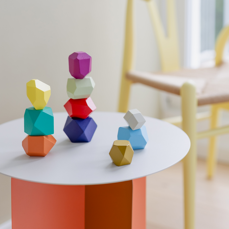 Colorful geometric wooden toys on a white table with a blurred chair in the background