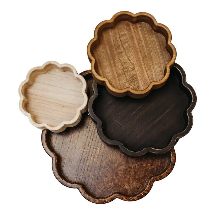 Set of four wooden trays with scalloped edges in various finishes on a white background