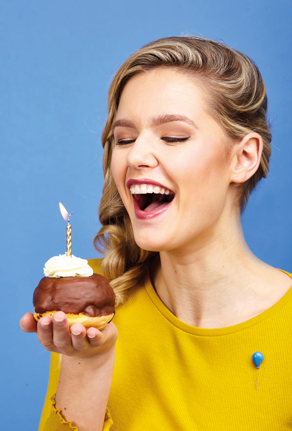 Woman holding a birthday donut with a candle against a blue background