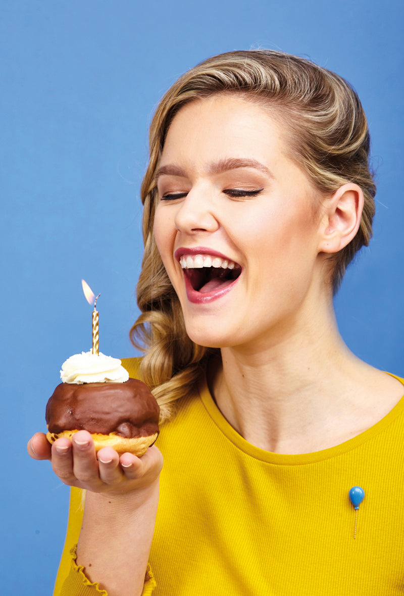 Woman holding a birthday donut with a candle against a blue background