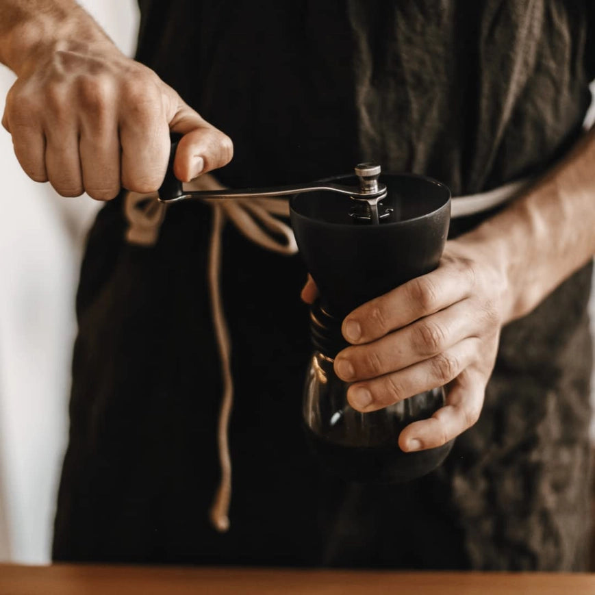 Person using a manual coffee grinder with a blurred background