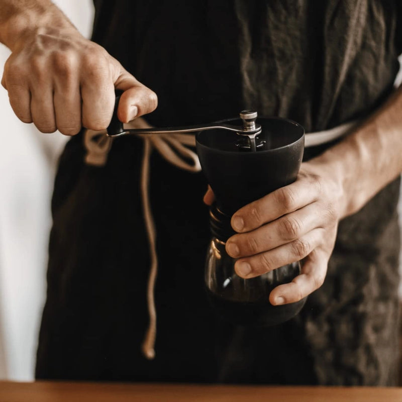 Person using a manual coffee grinder with a blurred background