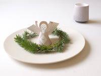 Decorative angel figure on a green wreath with a white candle on a white plate