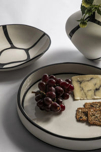 White ceramic plate with black rim displaying grapes, cheese, and crackers on a light background.