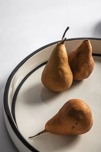 Three pears on a white plate with a black rim against a light background