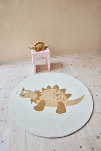 Round dinosaur rug on a wooden floor with a small pink stool and toy in the background.
