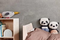 Two panda plush toys on a bed with a gray wall and wooden shelf in the background.