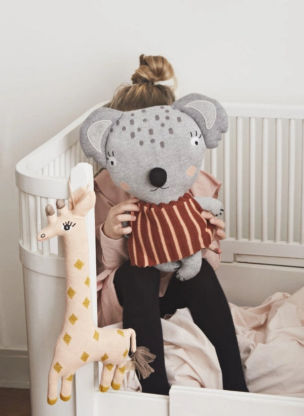 Child holding a plush koala toy in a crib with a giraffe toy nearby