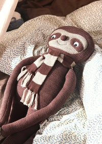 Knitted sloth toy with a scarf on a textured surface