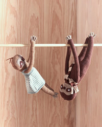 Two plush sloths hanging from a wooden bar on a wooden background