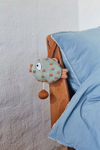 Knitted toy with brown spots hanging on a wooden hook against a white wall.