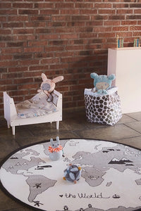 Children's room with a world map rug, toy bed, and teddy bears against a brick wall.