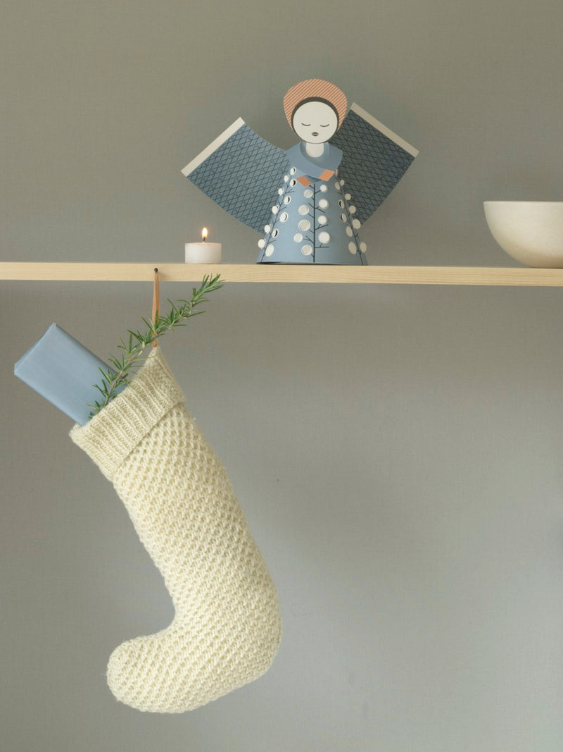 Knitted stocking hanging on a shelf with a decorative figure and candle in the background.