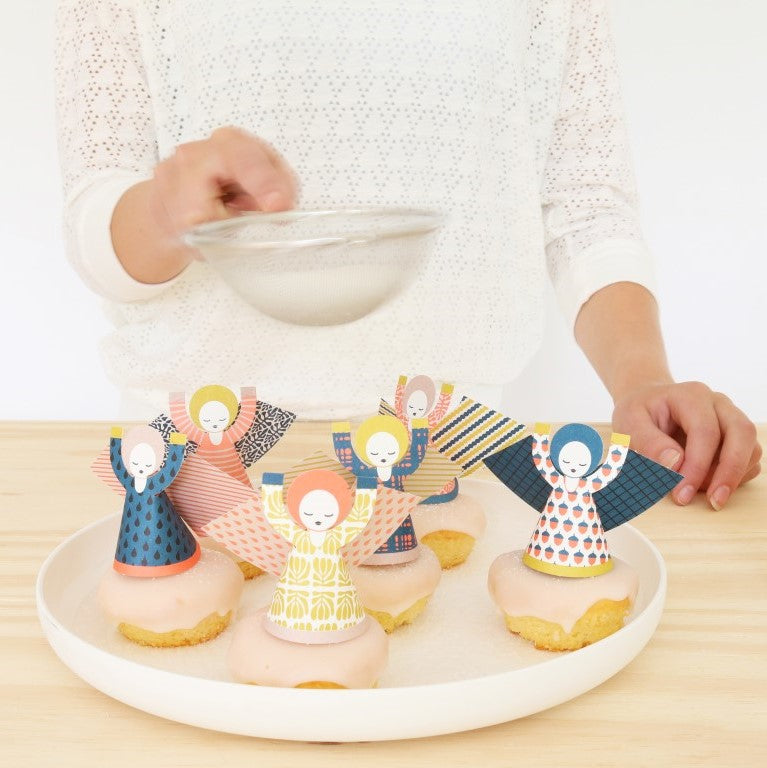 Decorative cookies shaped like people on a plate with a person holding a bowl in the background.