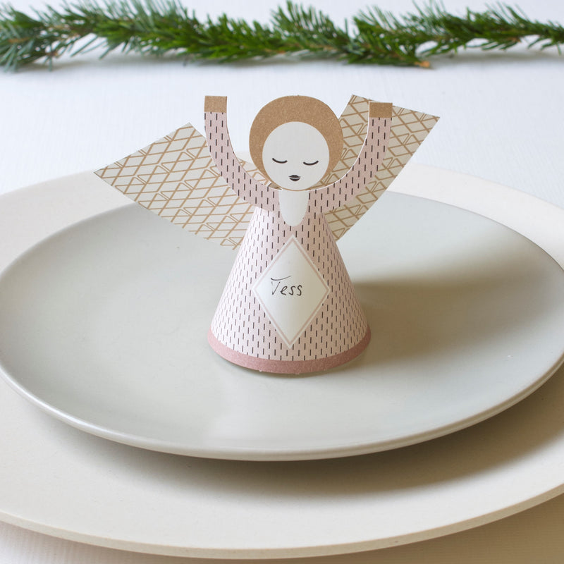 Decorative angel-shaped card on a stack of white plates with greenery in the background