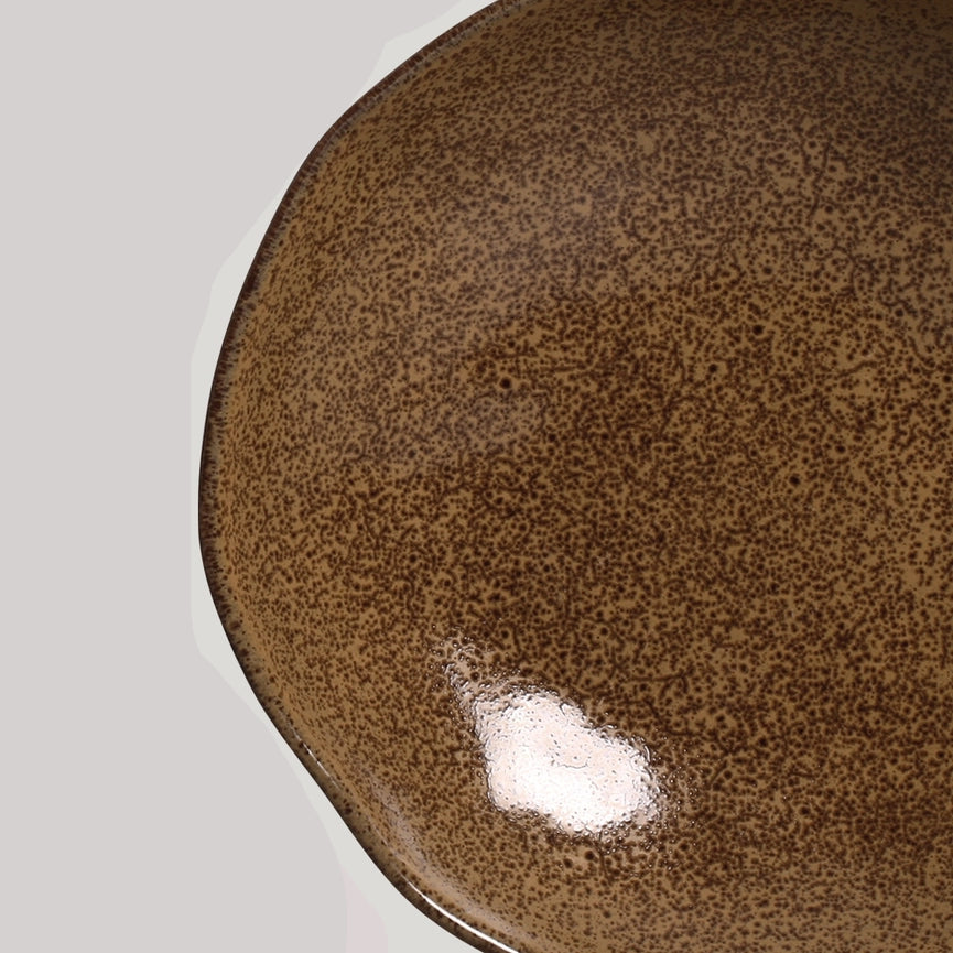 Close-up of a brown ceramic plate with reactive glaze on a light gray background