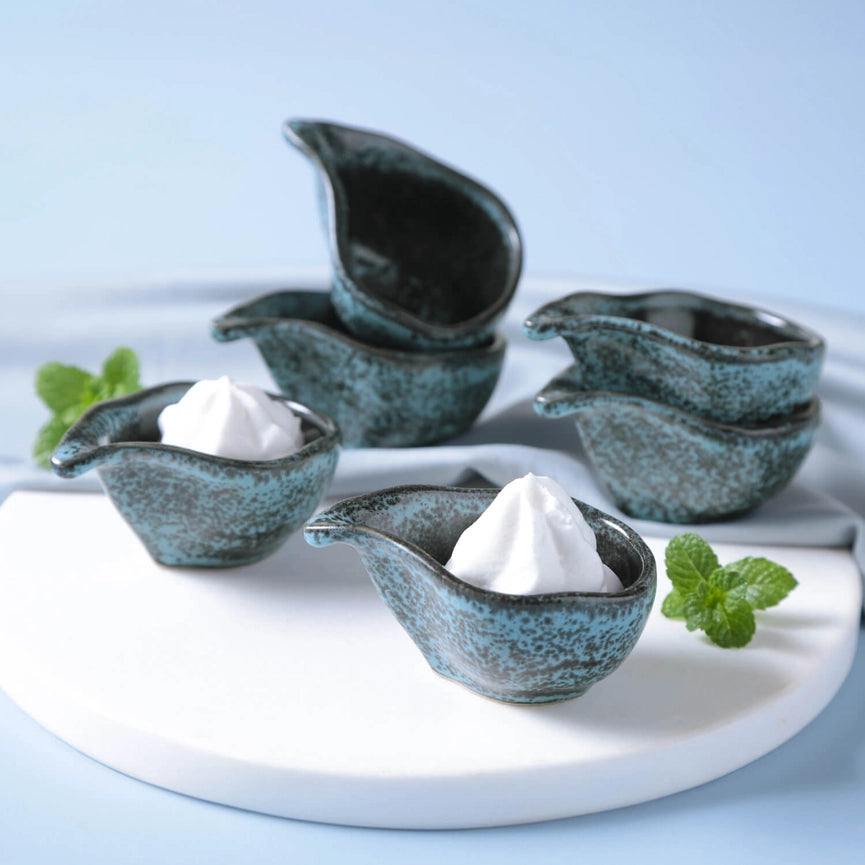 Set of ceramic condiment bowls with a white substance and mint leaves on a light blue background