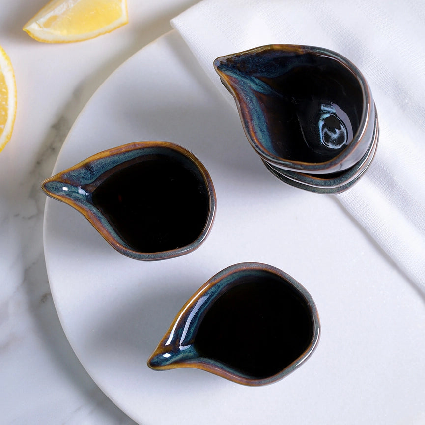 Three ceramic condiment containers filled with dark liquid on a white surface.