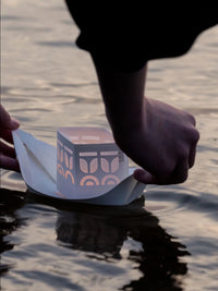 Person launching a paper boat with a geometric design into water