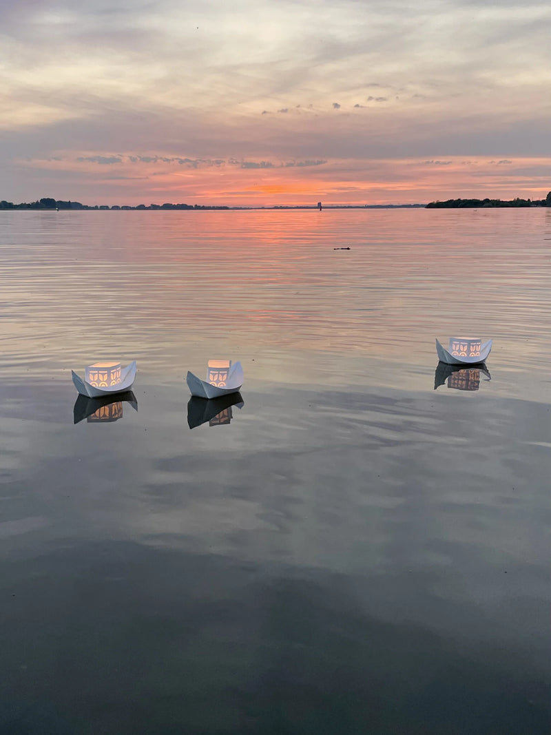 Three small boats floating on a calm lake at sunset.