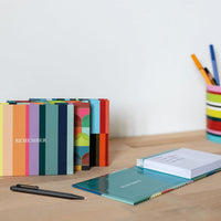 Colorful stationery items including notebooks and a pen on a wooden surface.