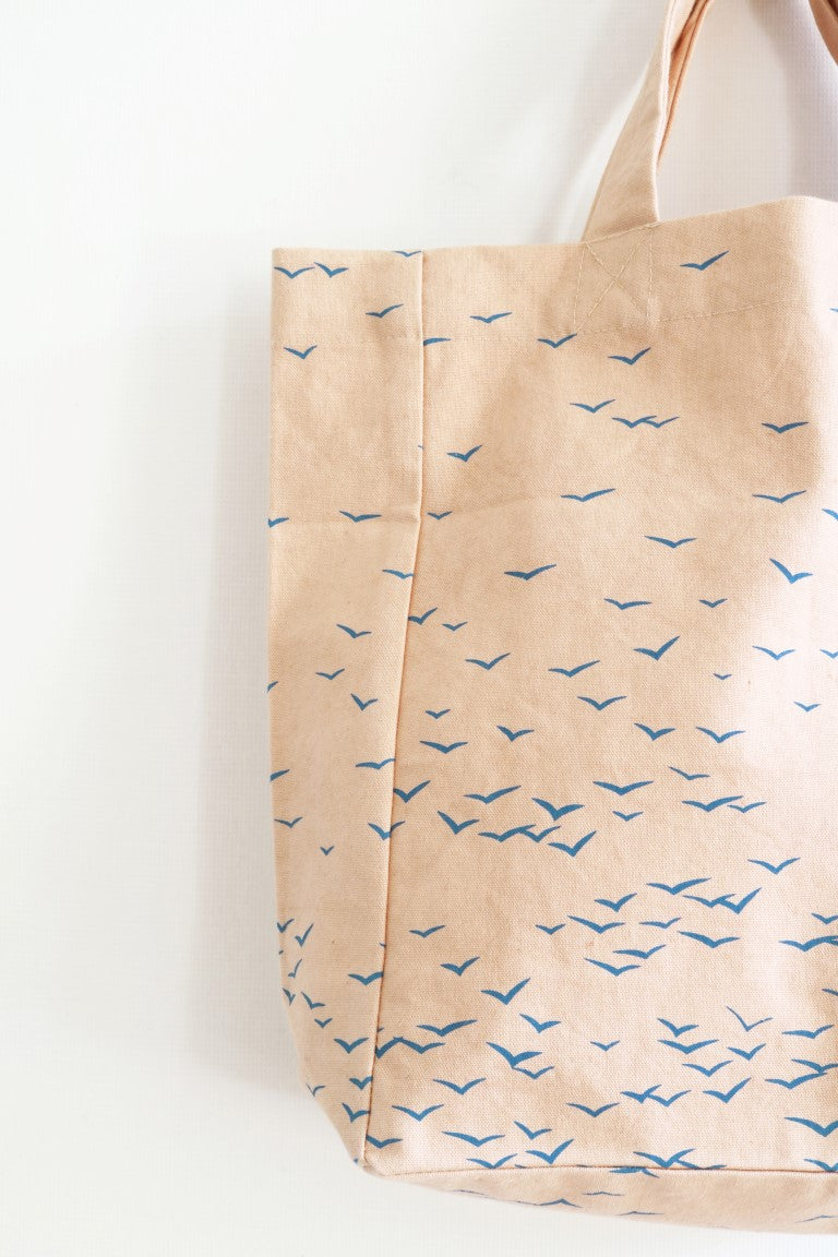 Beige tote bag with blue bird pattern on a white background