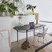 black oval desk with vses on it and a metal wire extra wide armrest chair