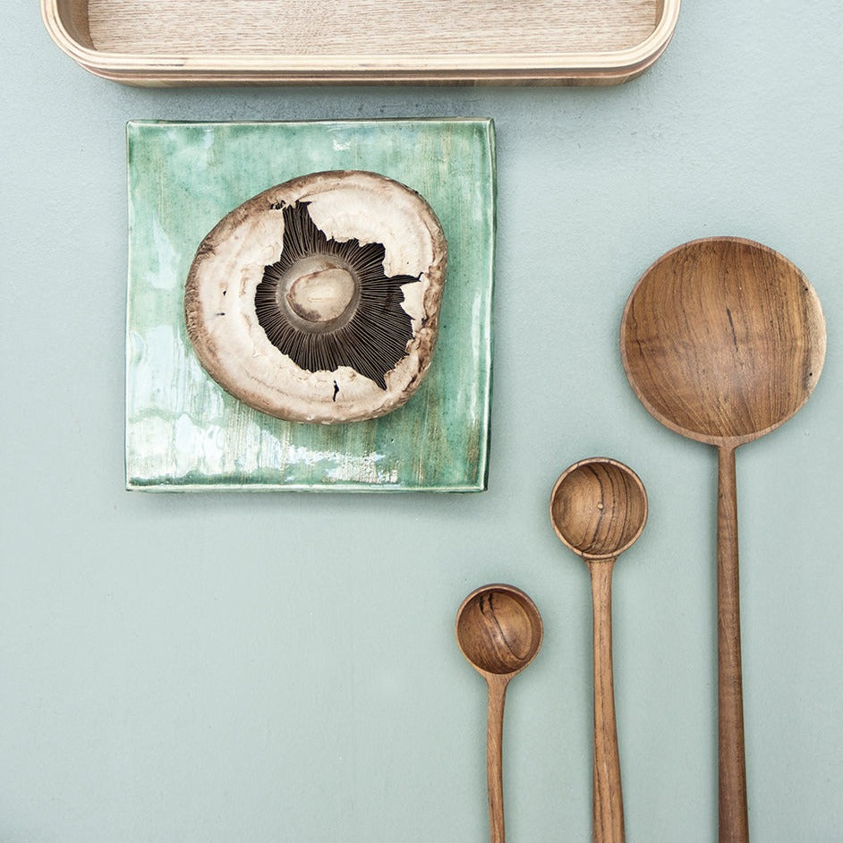 3 hand made wooden spoons on a green table top with a mushroom on a square green plate