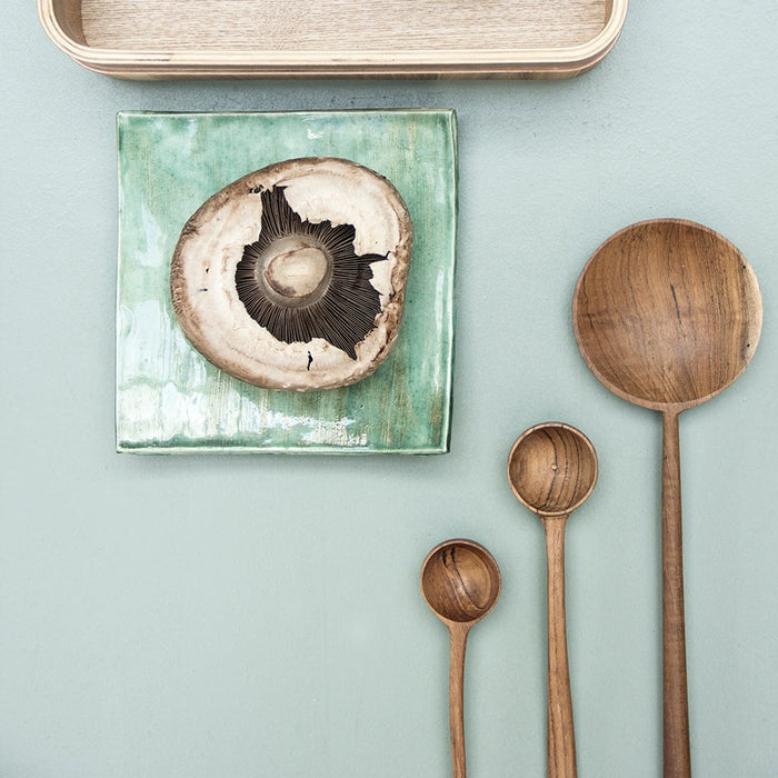 3 hand made wooden spoons on a green table top with a mushroom on a square green plate