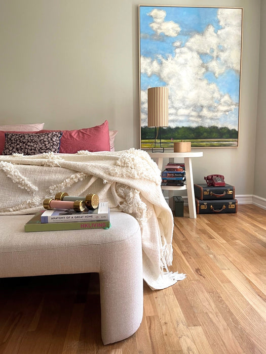 bedroom with natural linen bedding, upholstered bed bench and a large painting with clouds