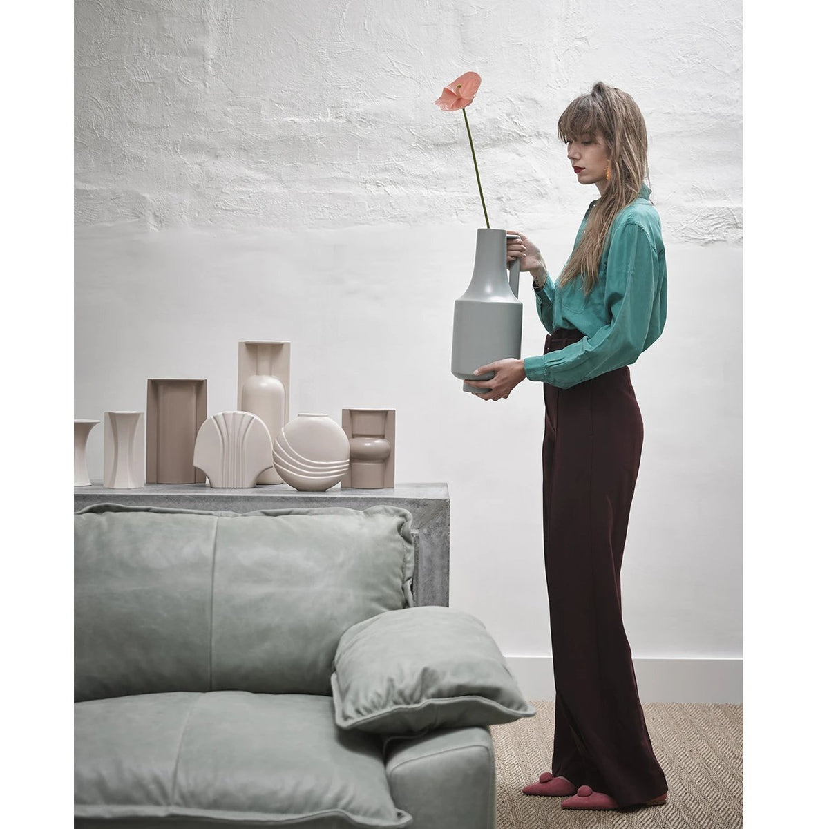 group of earthenware flowervases behind sofa and woman holding green vase