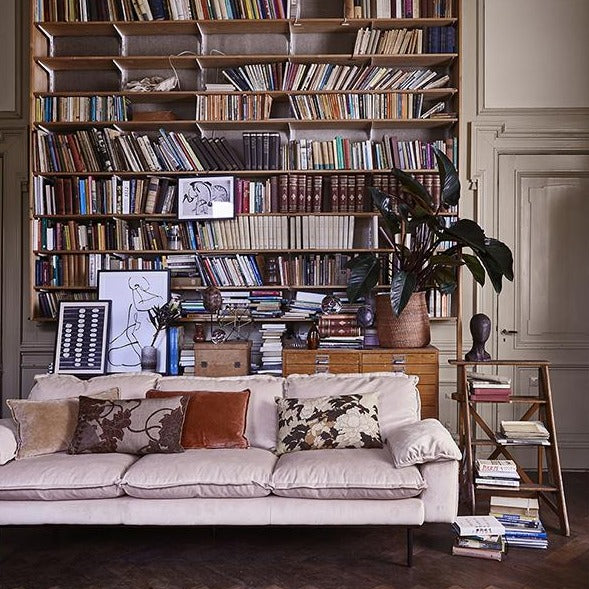 velvet couch in nude color in living room with large book shelf