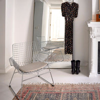 bedroom with large mirror with a dress hanging on top of and a metal wite chair with sand colored seating cushion on a vintage looking rug