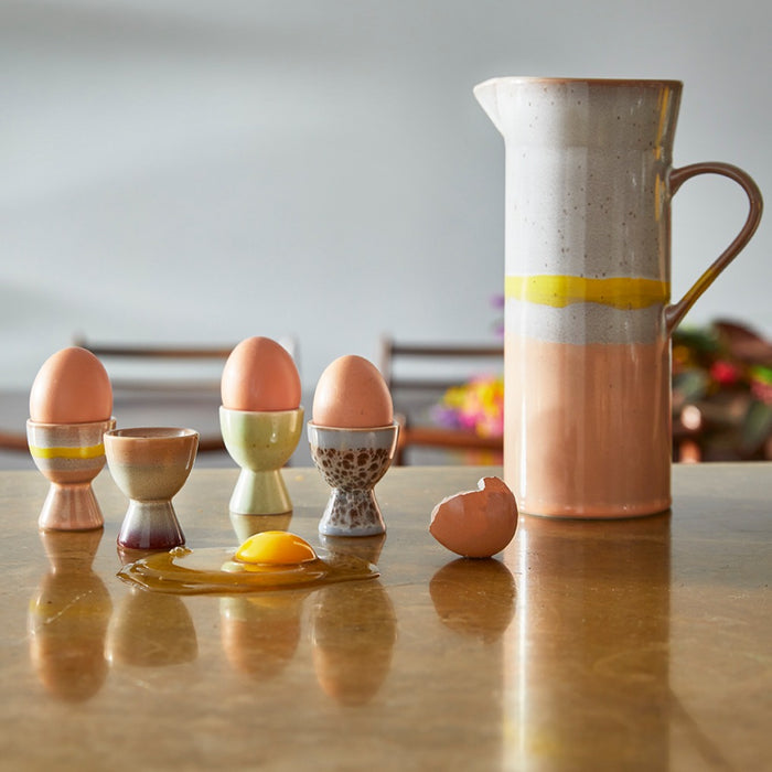 egg cups in soft pastel colors on a table with a large ceramic jug