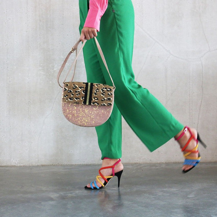 blush colored shoulder bag with panther print and golden speckles, carried by a woman with green pants
