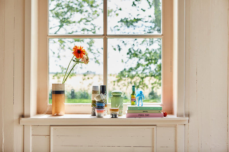 cream brown and orange peach colored tall retro style flower vase next to retro style coffee cups and a stack of books